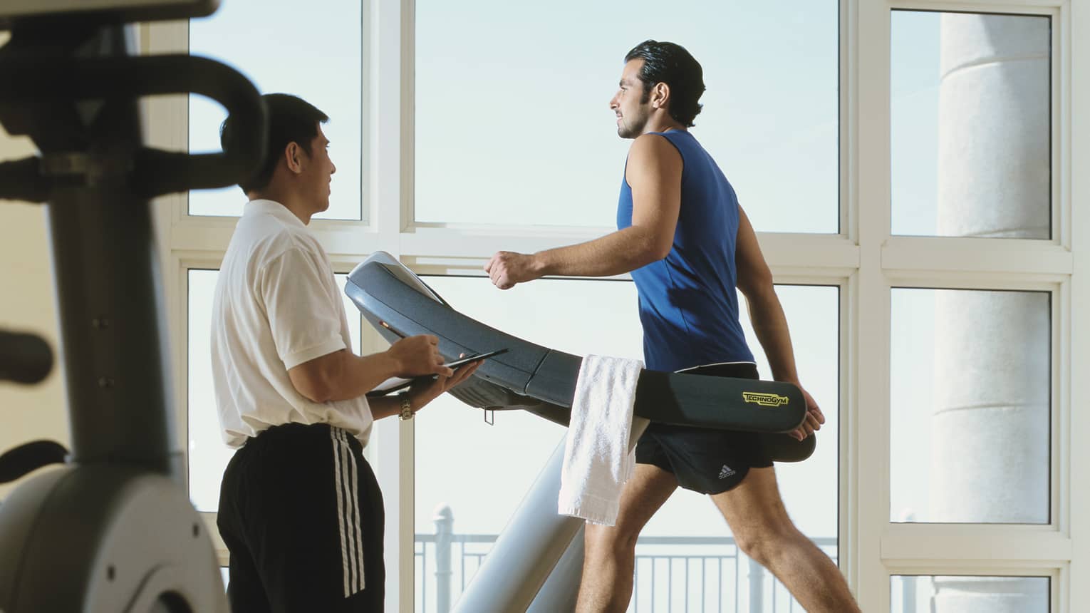 Man in workout gear on treadmill as personal trainer looks on