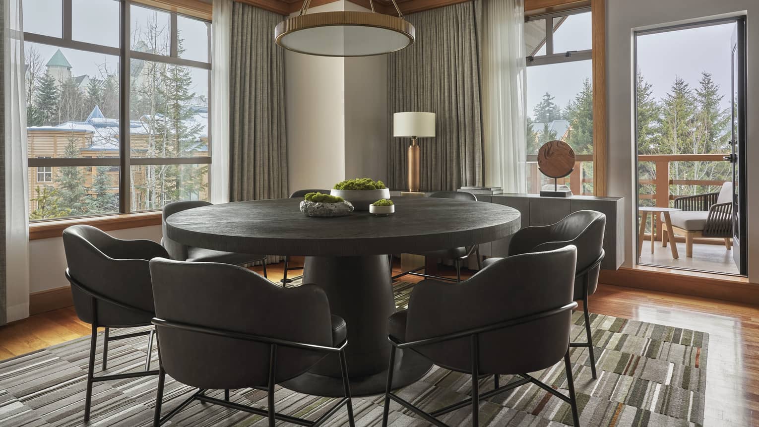 Round dining table with six modern, leather seats and a door leading out to a balcony