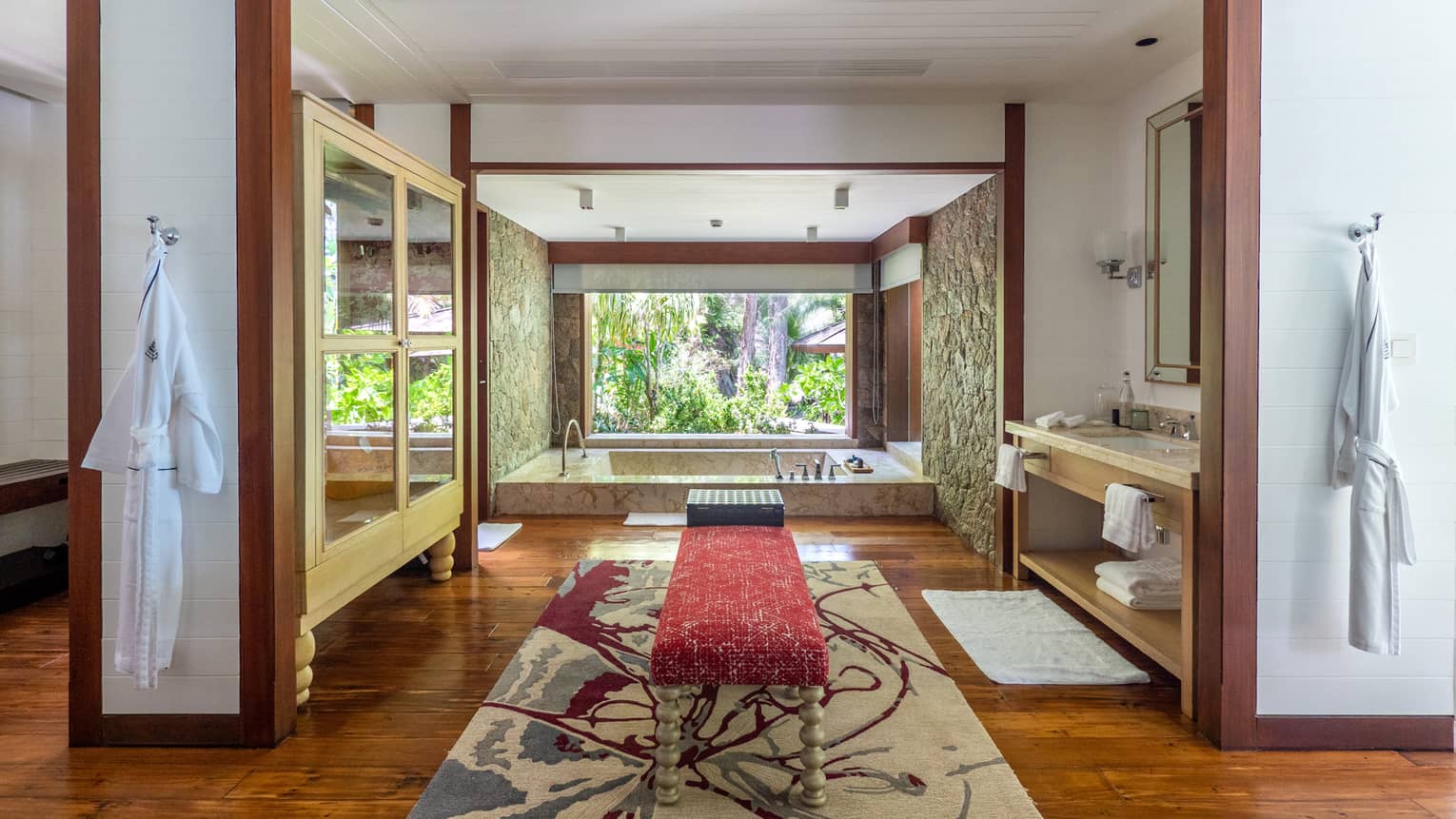 Lavish large bathroom with bench in the middle, sunken tub and window with tropical view