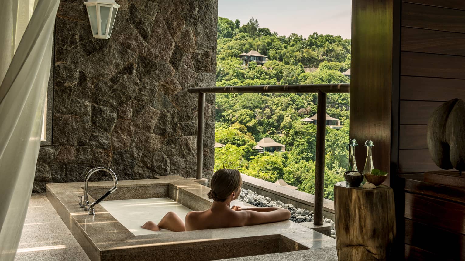 Back of woman sitting in rectangular hot tub, looking out open wall at mountain