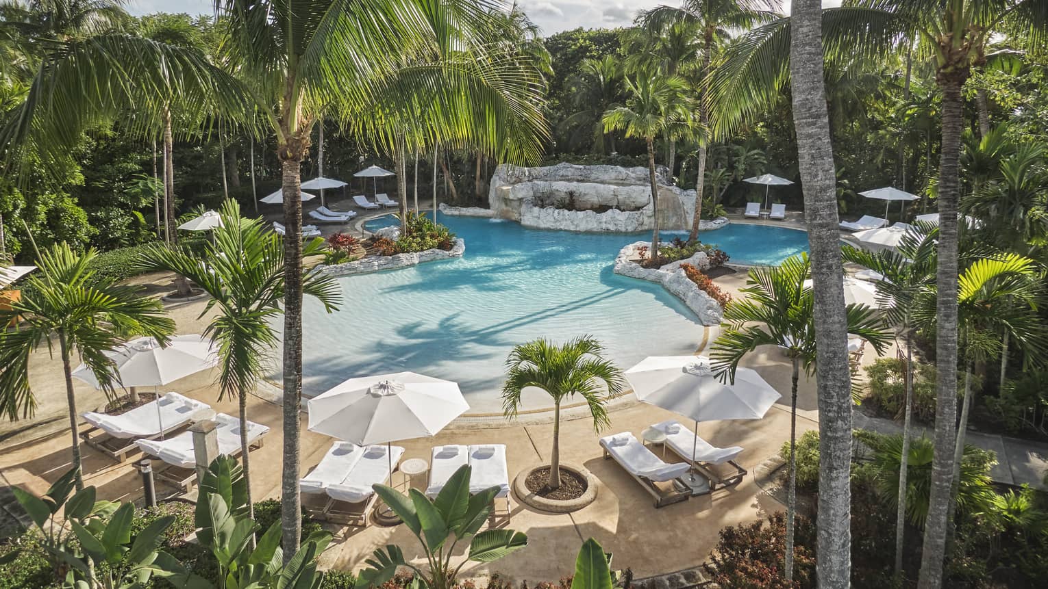 An outdoor pool surrounded by white lounge chairs and palm trees.