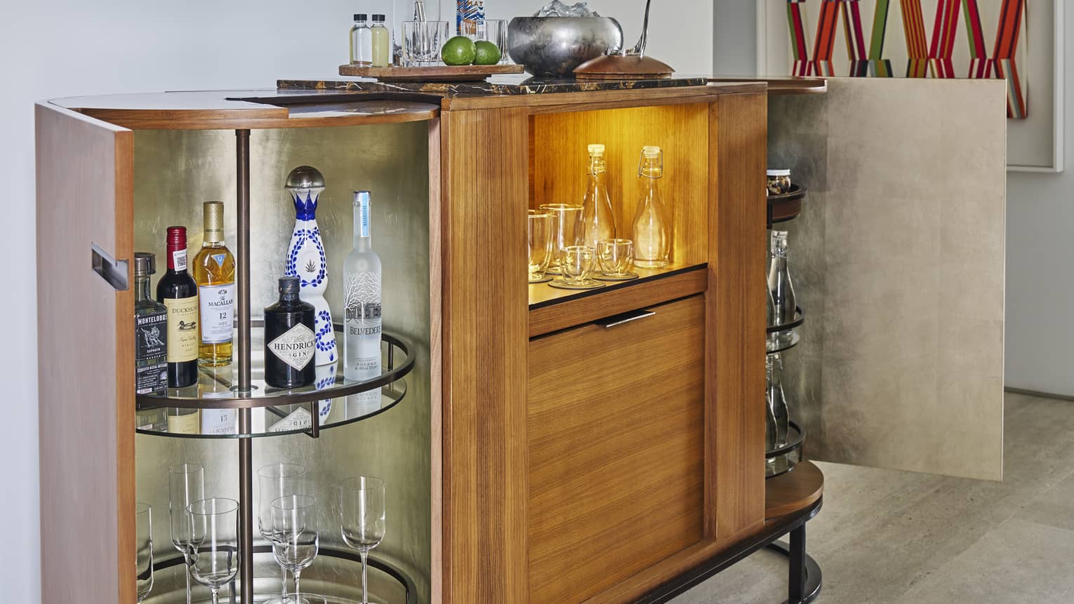 Stylish minibar cupboards open to show liquor bottles and white glasses in a luxury hotel room