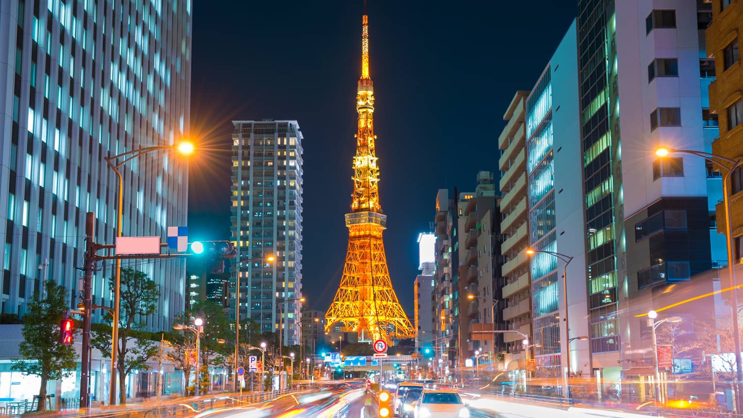 Long view down a brightly-lit street, the Tokyo Tower at the bottom, glowing in orangey hues against an inky-black sky.