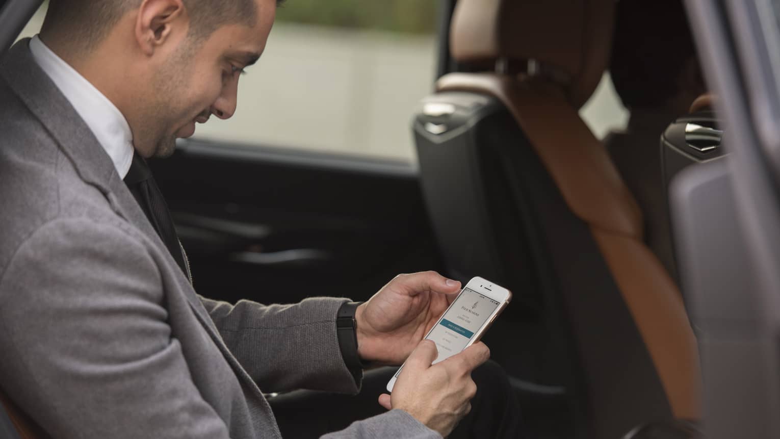 Man in suit sitting in backseat of car, holding cell phone