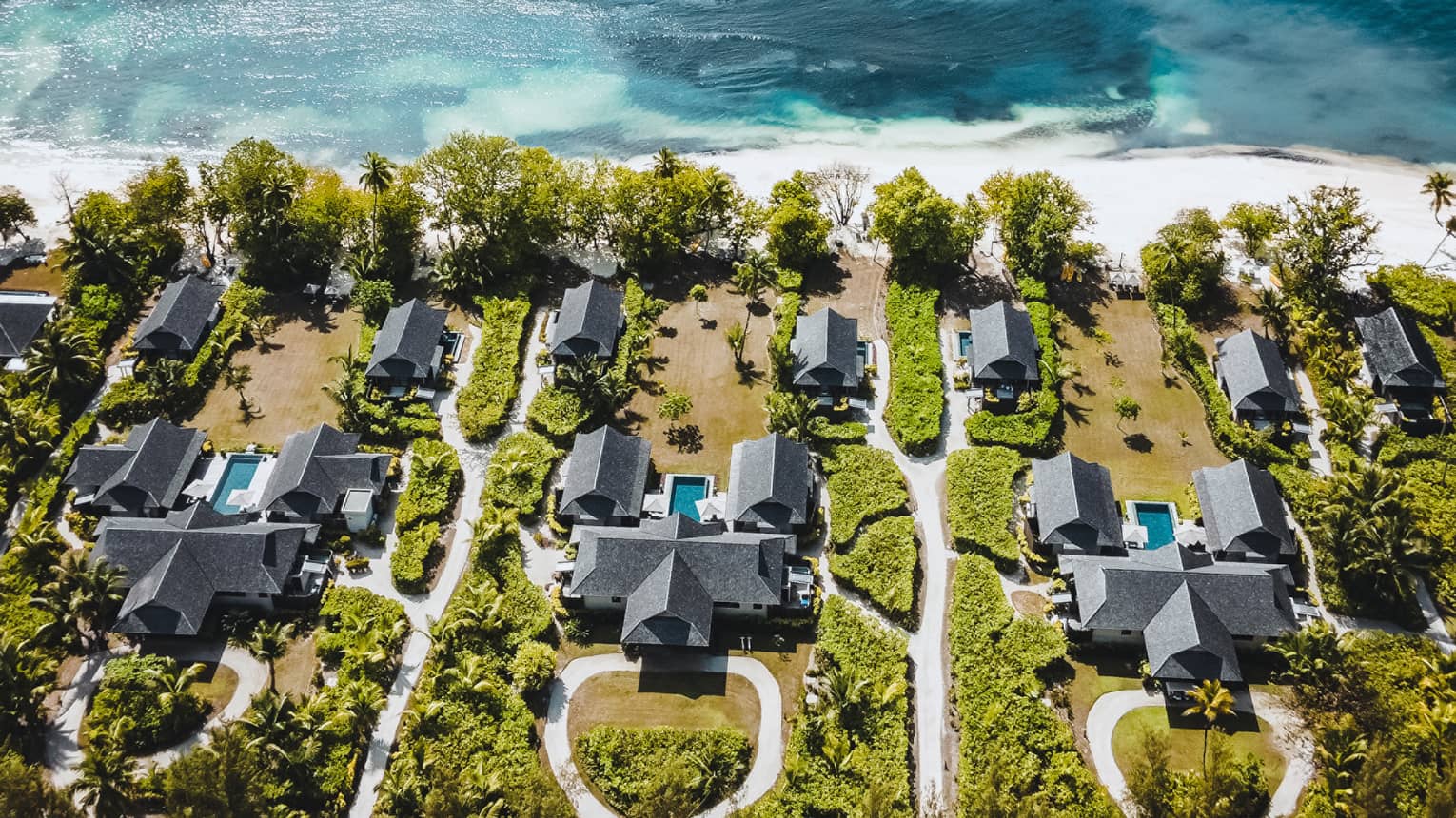 Aerial view of villas amidst greenery, facing the ocean