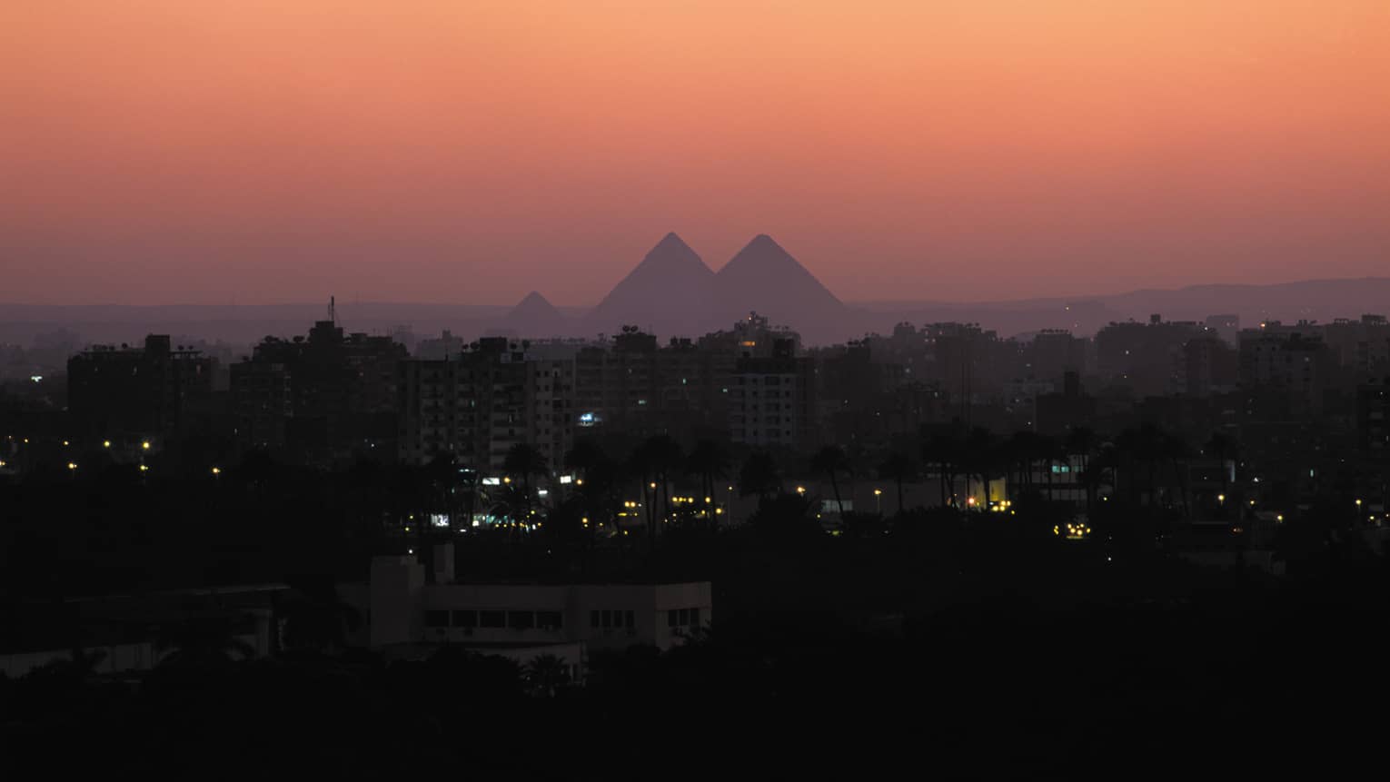 Silhouettes of the Great Pyramids of Giza against a pink sunset