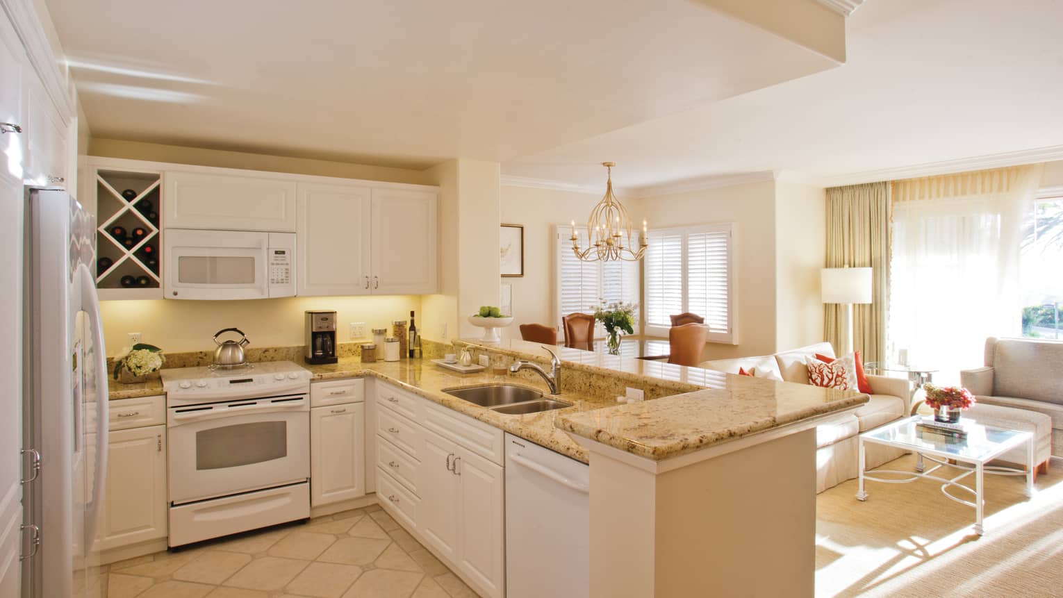 Villa kitchen with stove, dishwasher, cupboards under L-shaped marble counter, overlooking living room