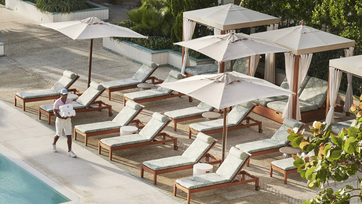 Poolside lounge chairs and umbrellas with a hotel team member carrying towels.