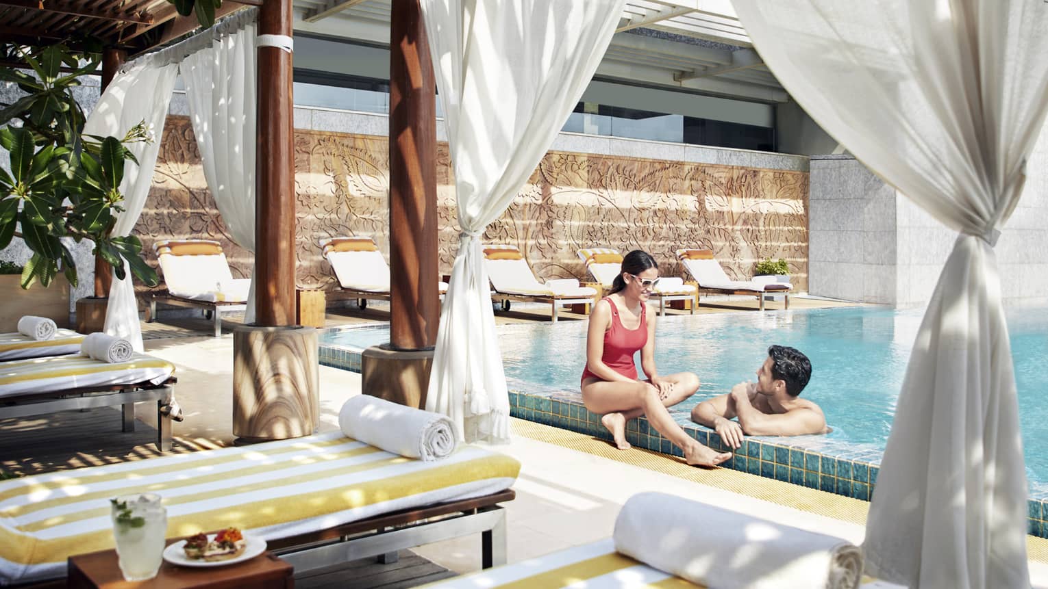 A couple lounges in the pool near a shaded cabana with fresh fruit