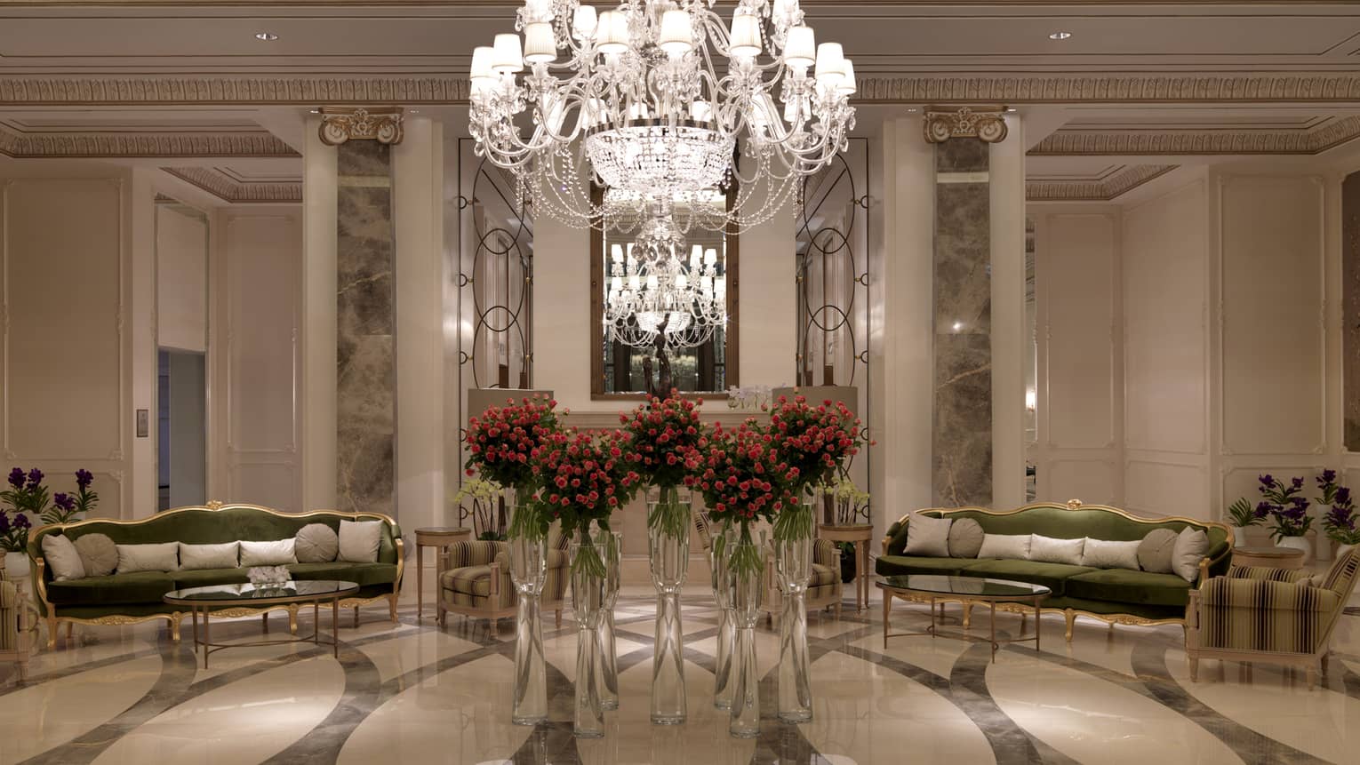 Foyer with large crystal chandelier over flowers in vases, velvet sofas