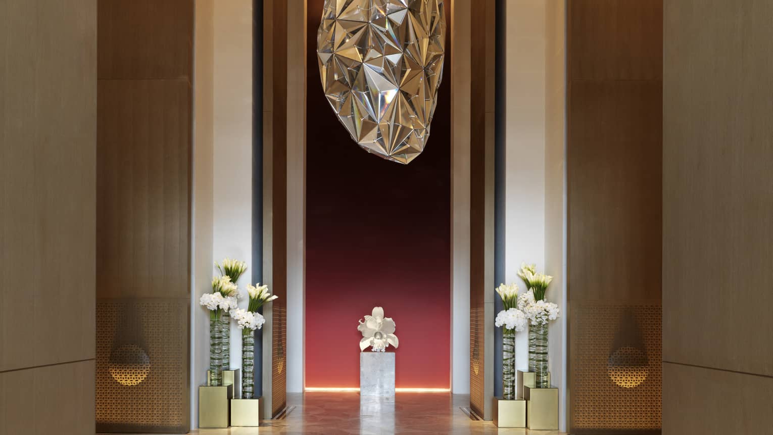 Large silver sculpture hanging above marble floors, tall vases with fresh white flowers