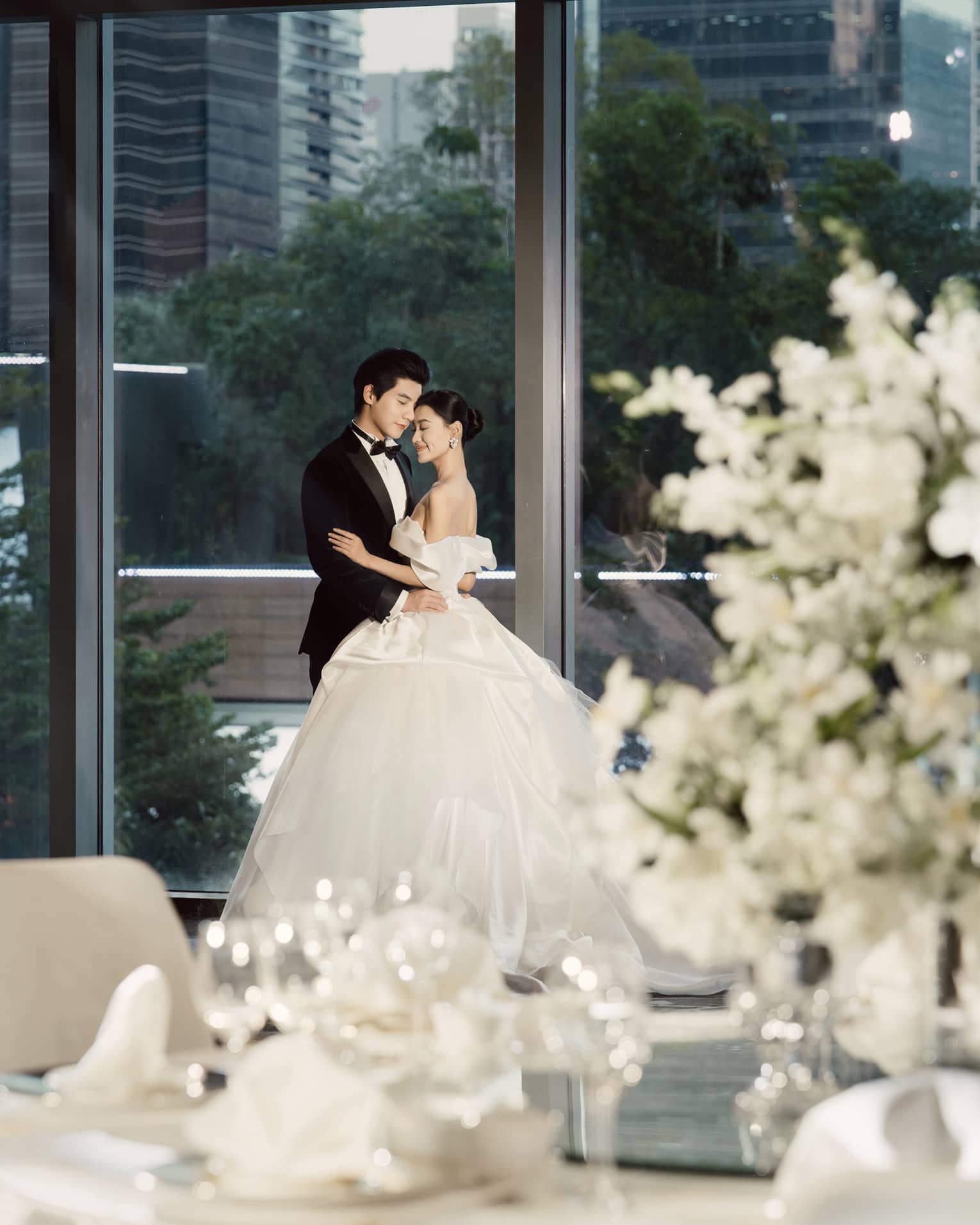 Bride and groom embrace in ballroom with floor-to-ceiling windows