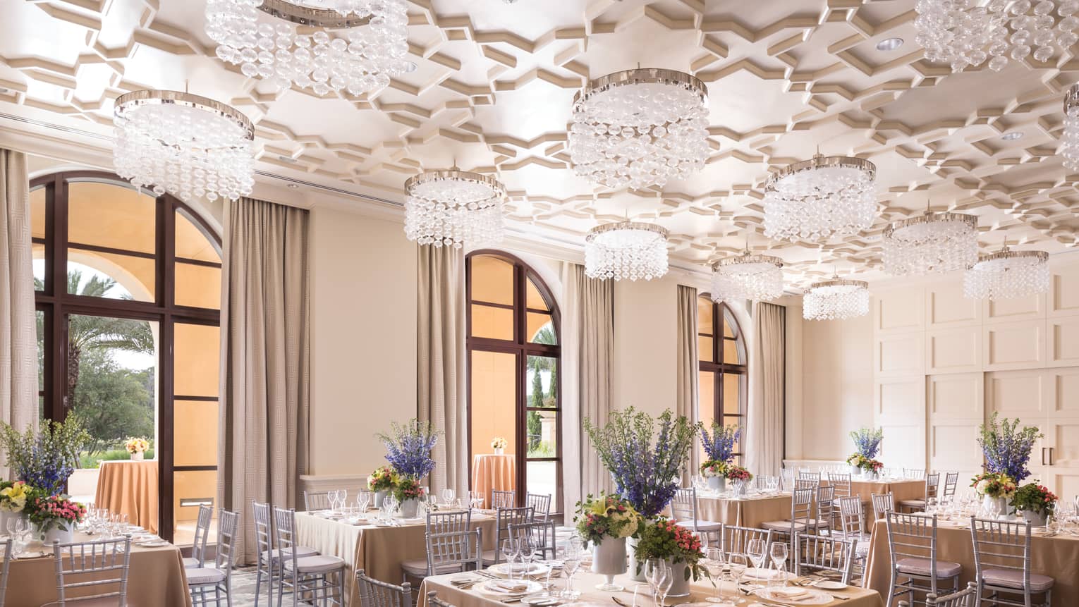 Square banquet dining tables under geometric ceiling with crystal chandeliers 