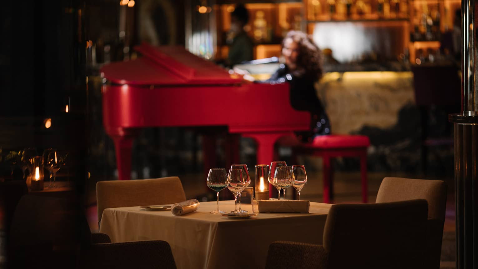 Pianist at red baby grand in backdrop of dimly lit restaurant lounge