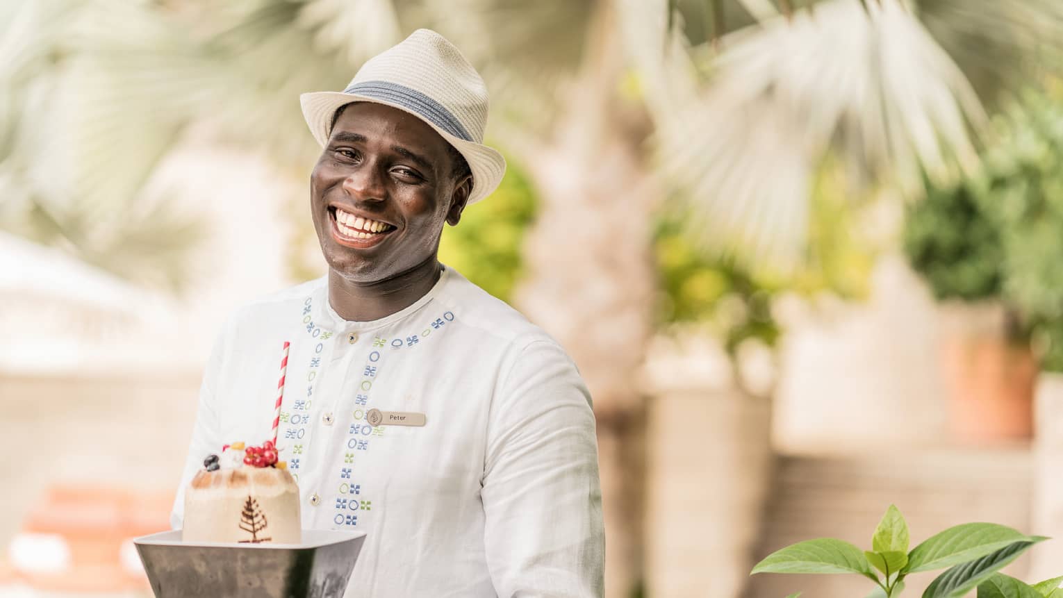 Pool staff member in white tunic and fedora holding ice cream dessert with striped straw