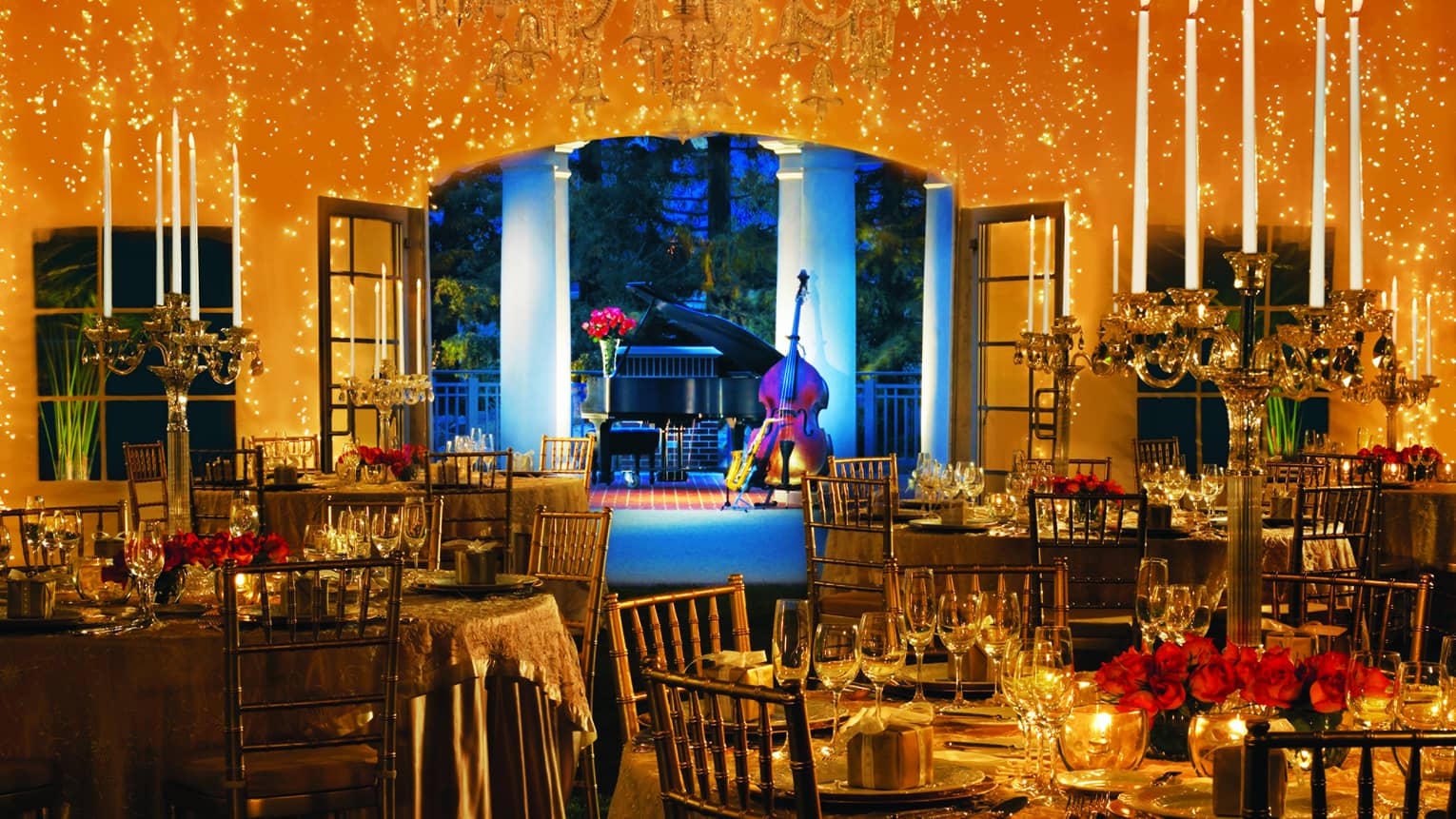 Interior of garden tent with dining tables, candelabras, red roses, romantic lighting, overlooking musical instruments 