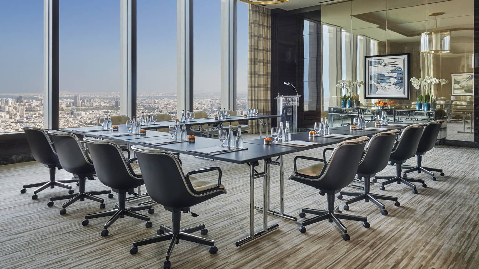 Meeting room with glass modular table lined with swivel chairs, floor-to-ceiling glass windows