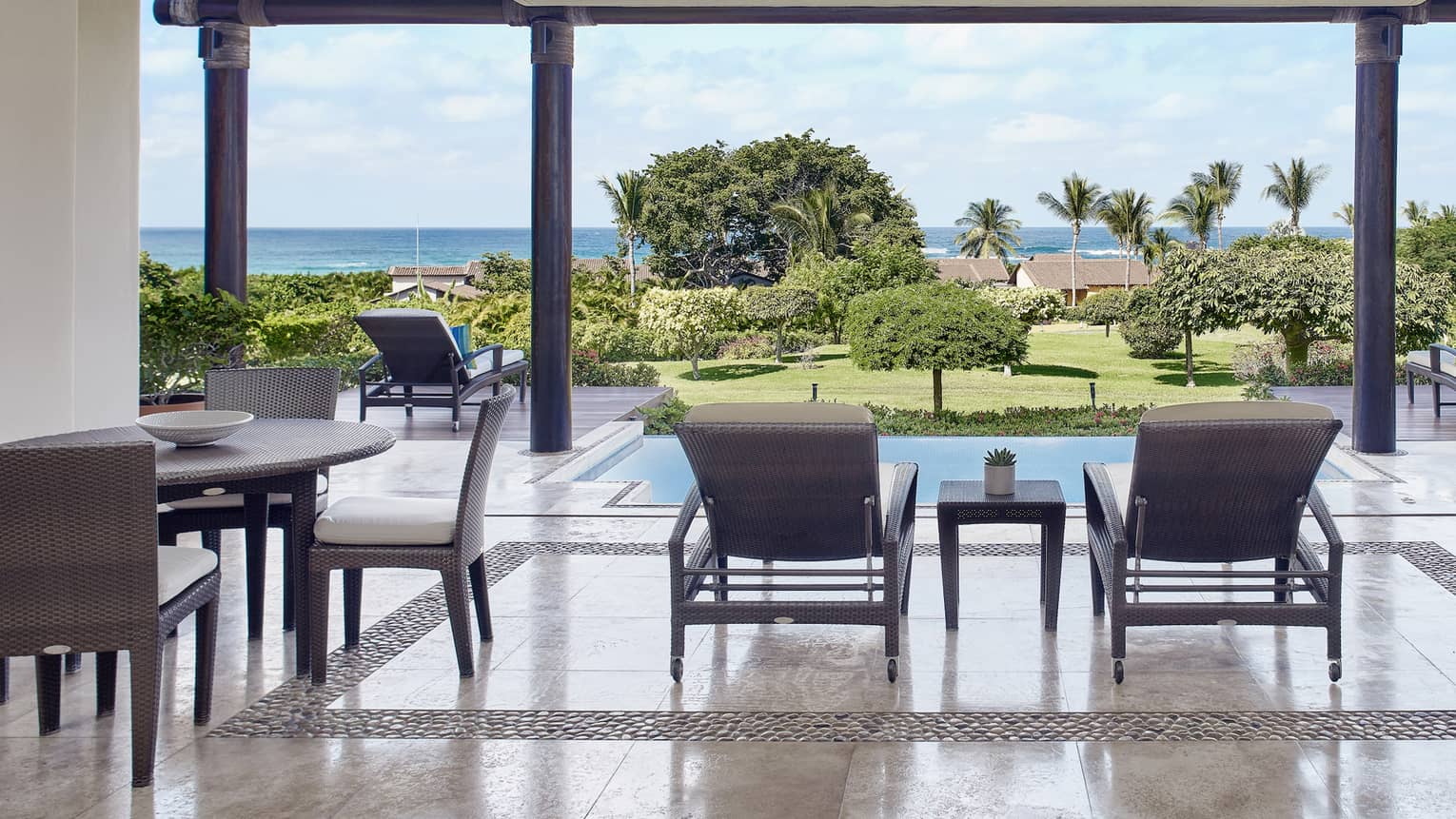 Terrace with dining table and lounge chairs, looking out to private pool and ocean in the distance