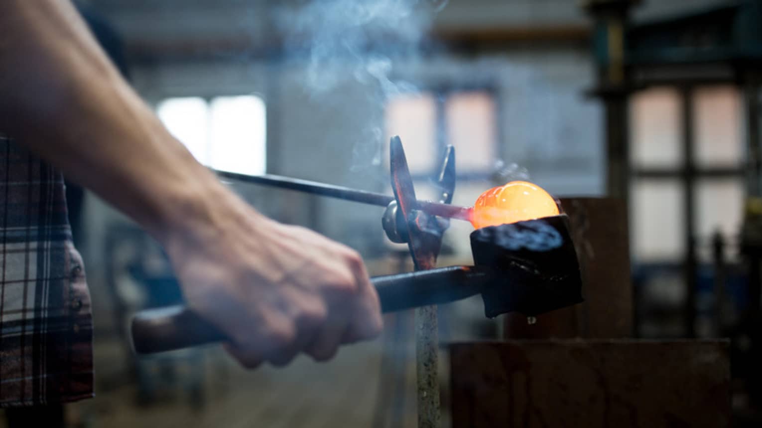 A person holding tools to hold molten glass.