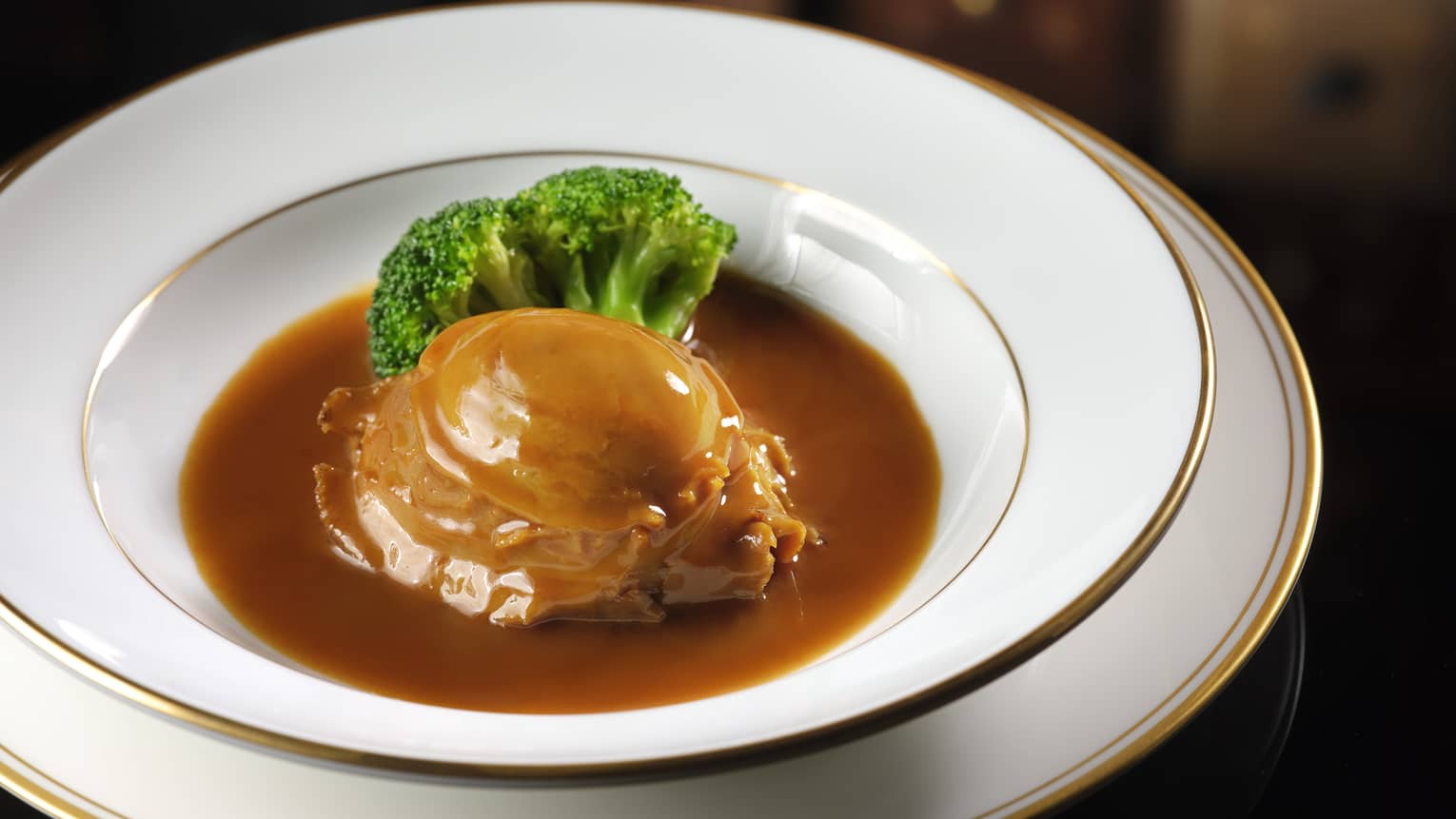 Gold rimmed white bowl with entree, brown sauce and broccoli