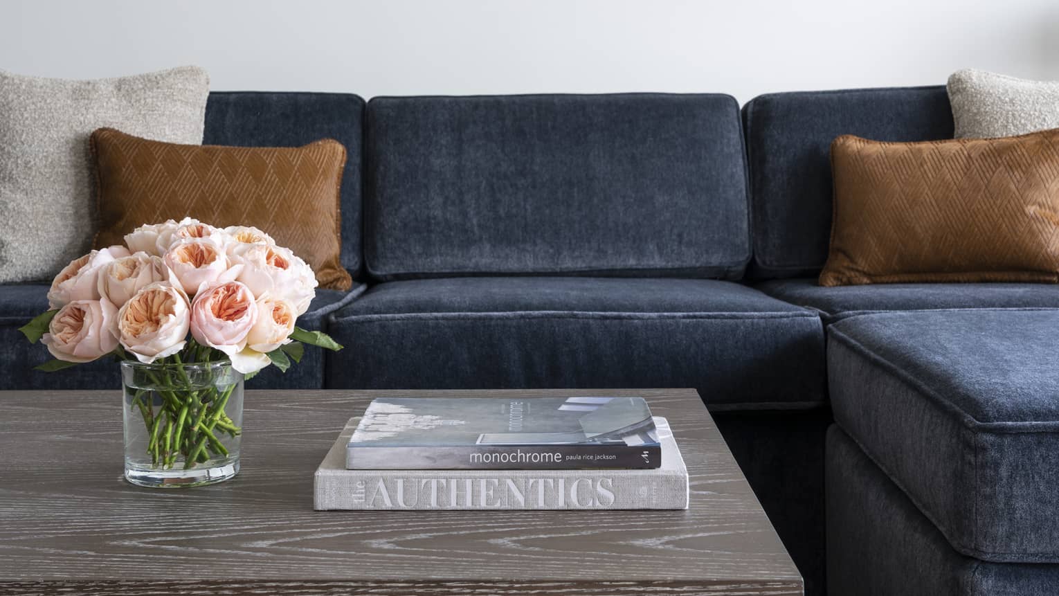 A blue couch near a grey coffee table with books and flowers on it.