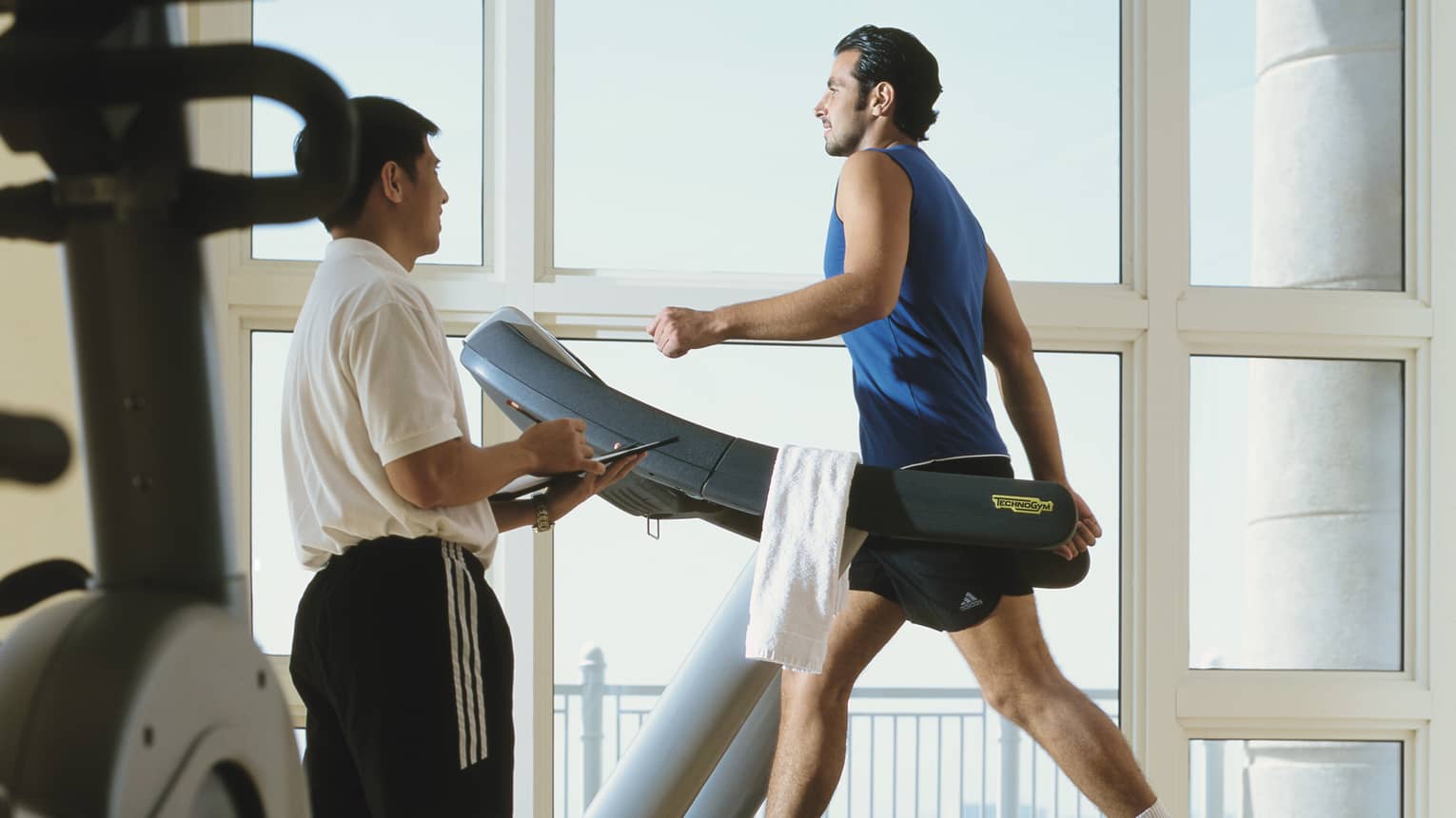 Man in workout gear on treadmill as personal trainer looks on