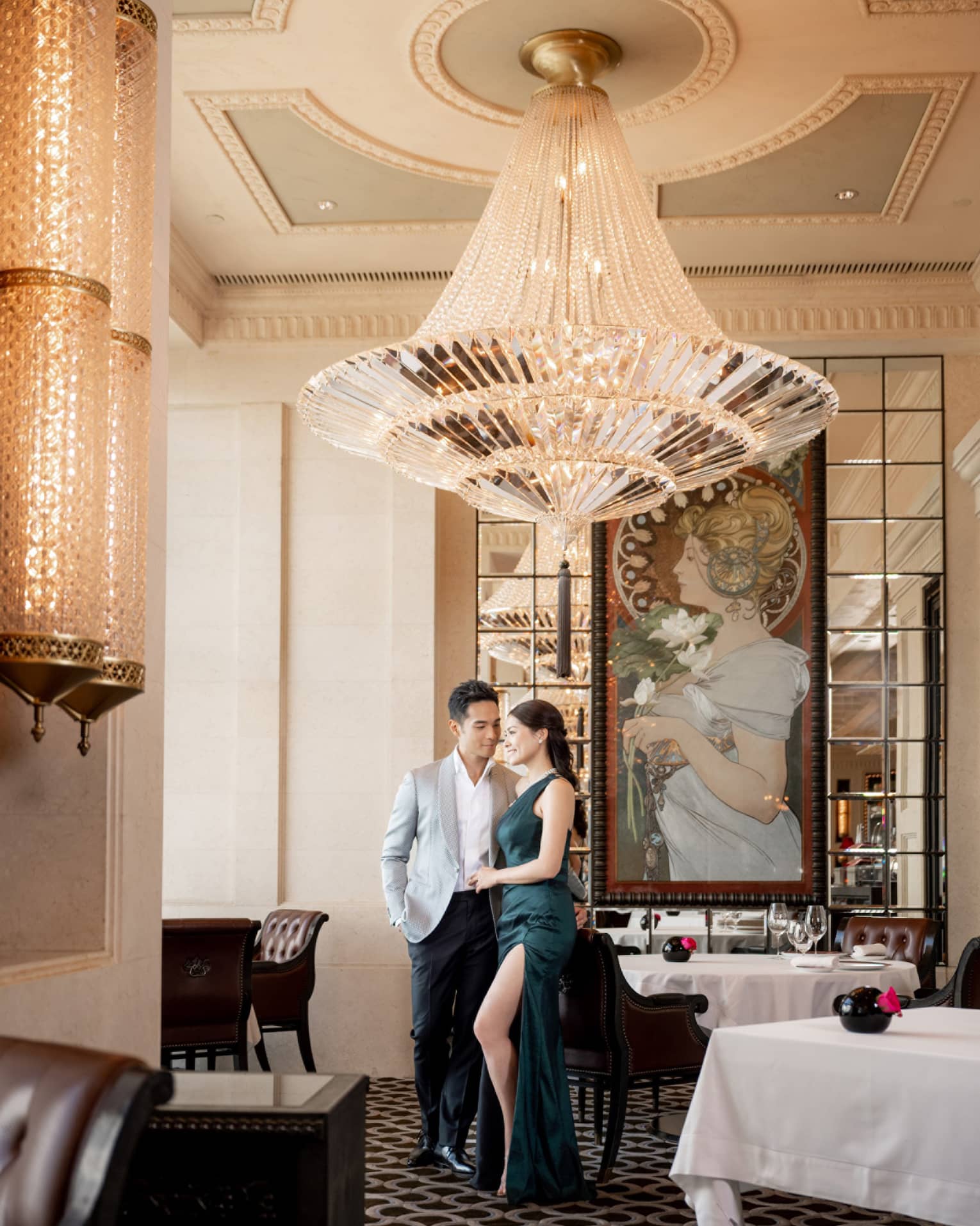 A man and woman in a suit and dress under a large chandelier in a dining outlet.