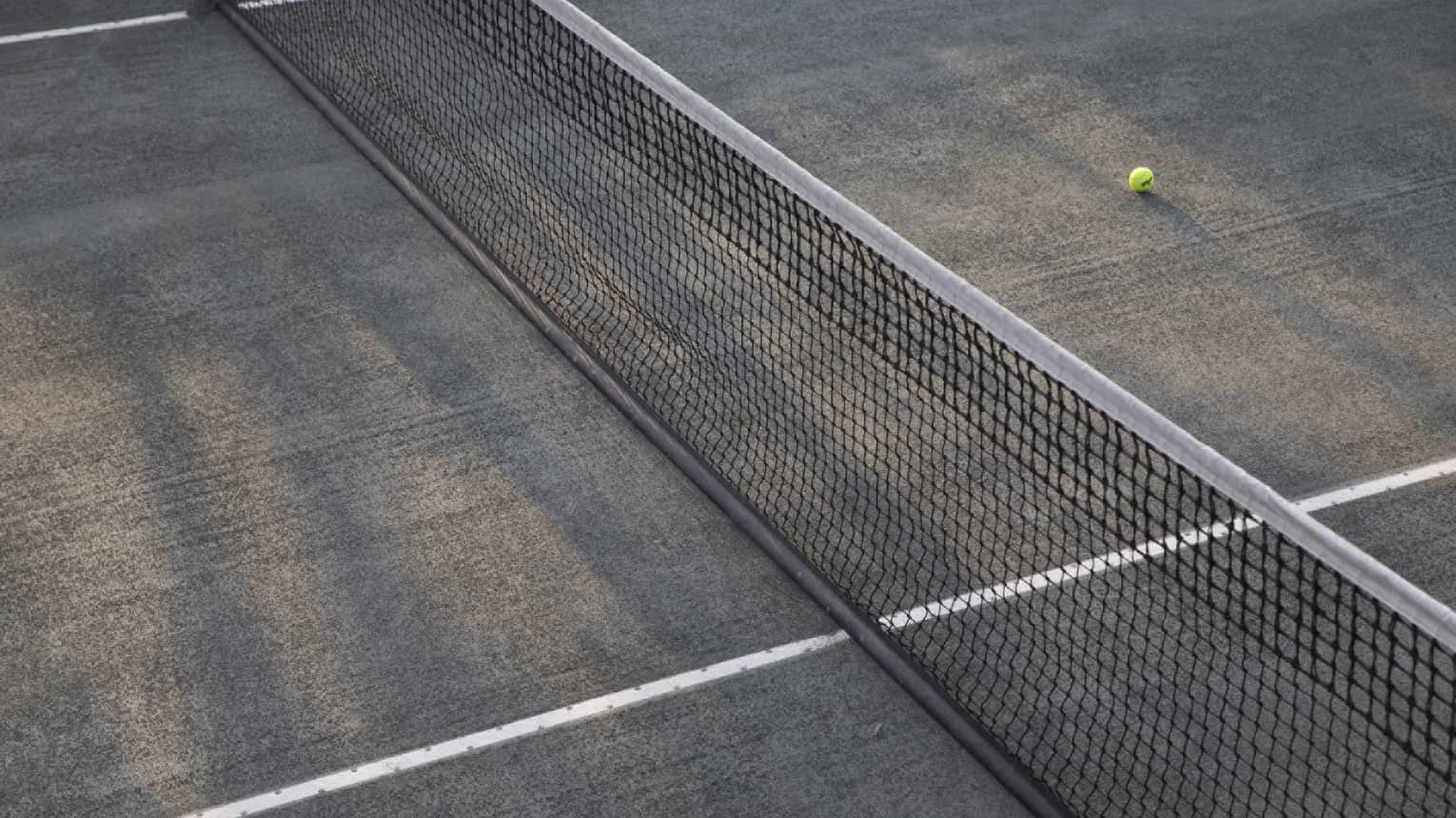 A lone tennis ball lies near the net on an empty court