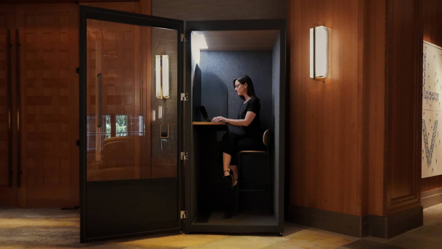 Woman sits in a glass-walled and sound-proofed virtual office room