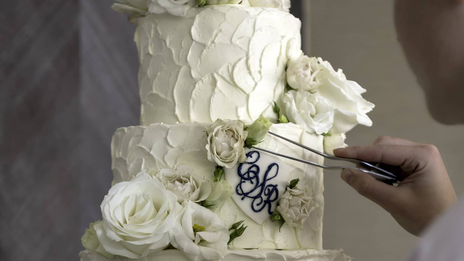 Chef places rose garnish on four tier white wedding cake