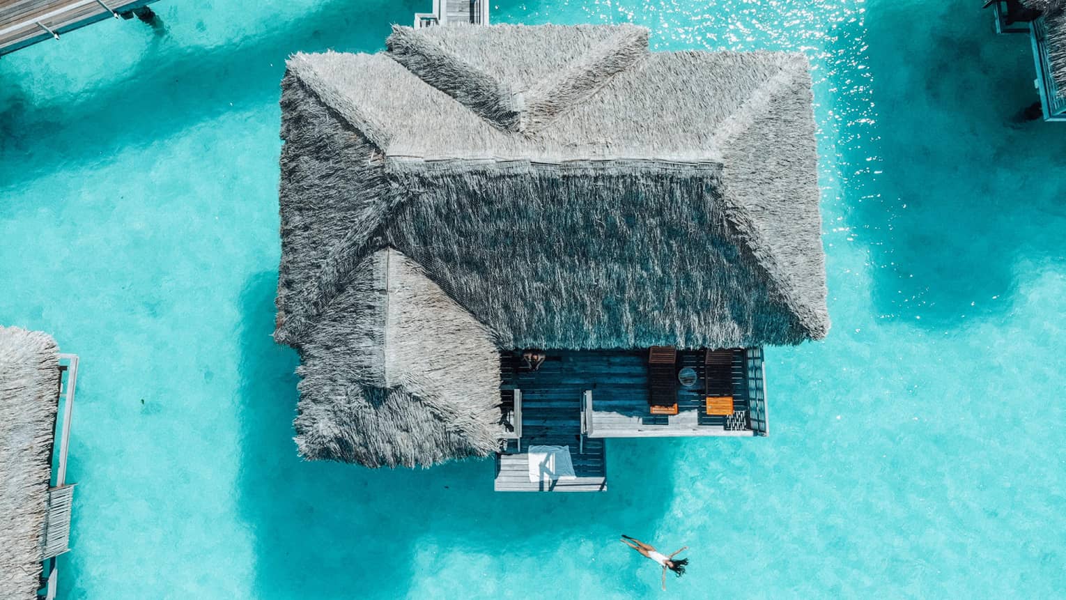 Aerial view of person swimming away from overwater bungalow in turquoise lagoon