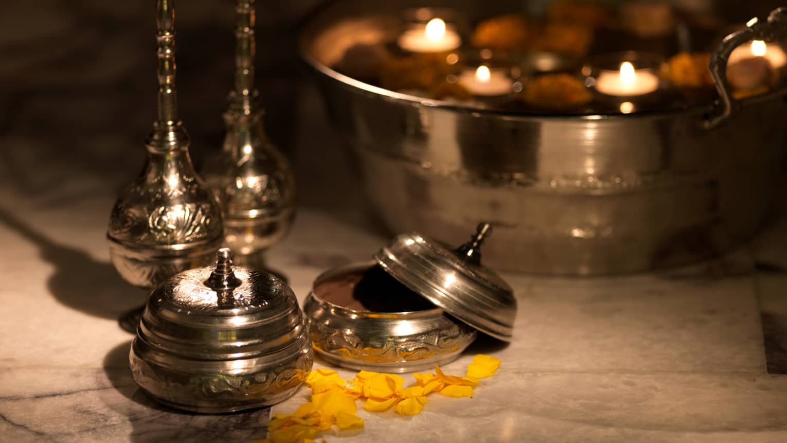 Spa ingredients lay on table with metal containers, a bowl with floating votive candles