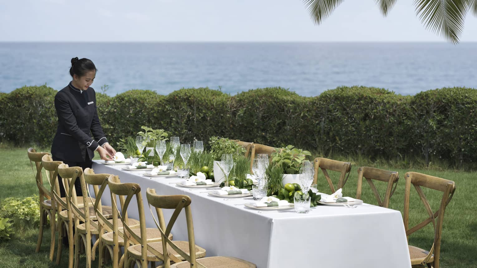 A four Seasons staff setting an outdoor table with wooden chairs overlooking the ocean