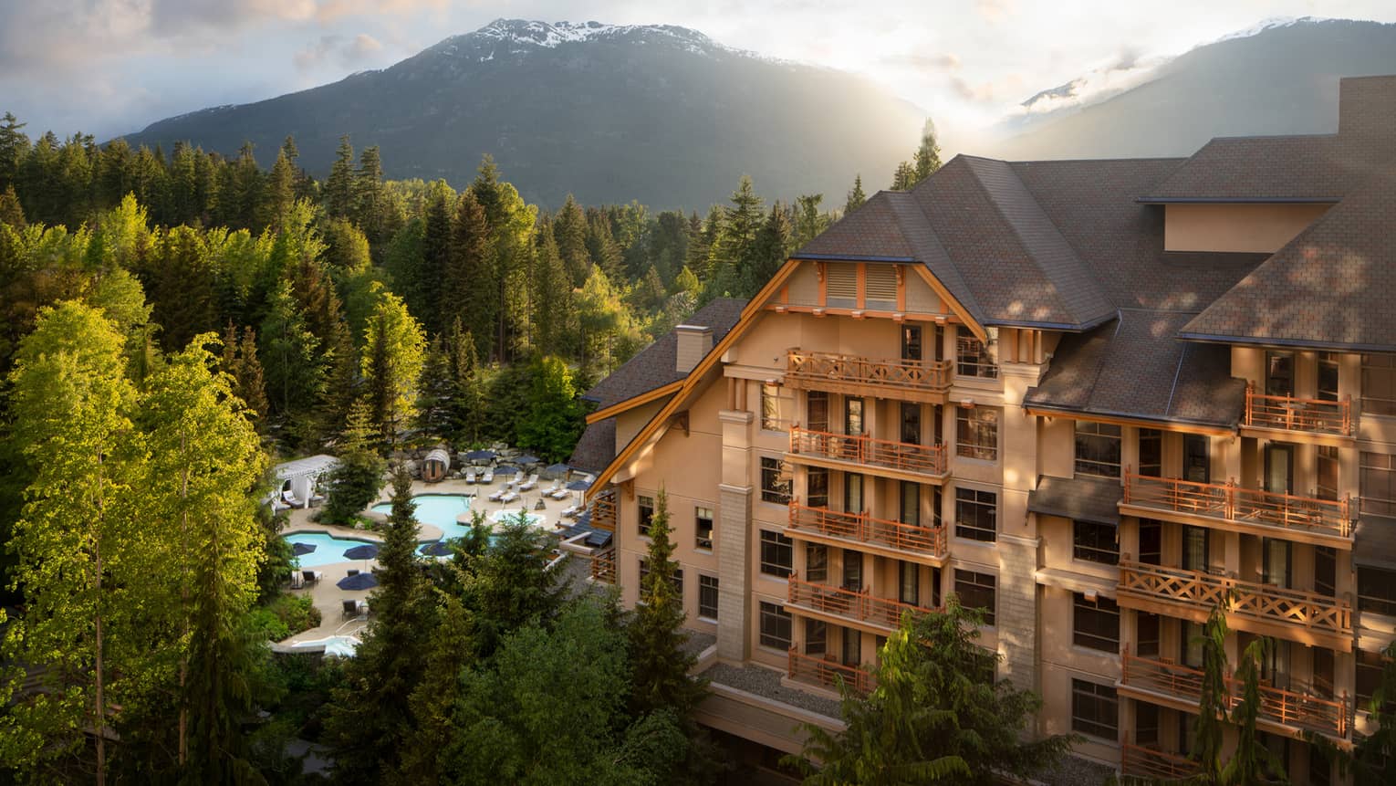 A large hotel building surrounded by mountains and trees during sunrise.