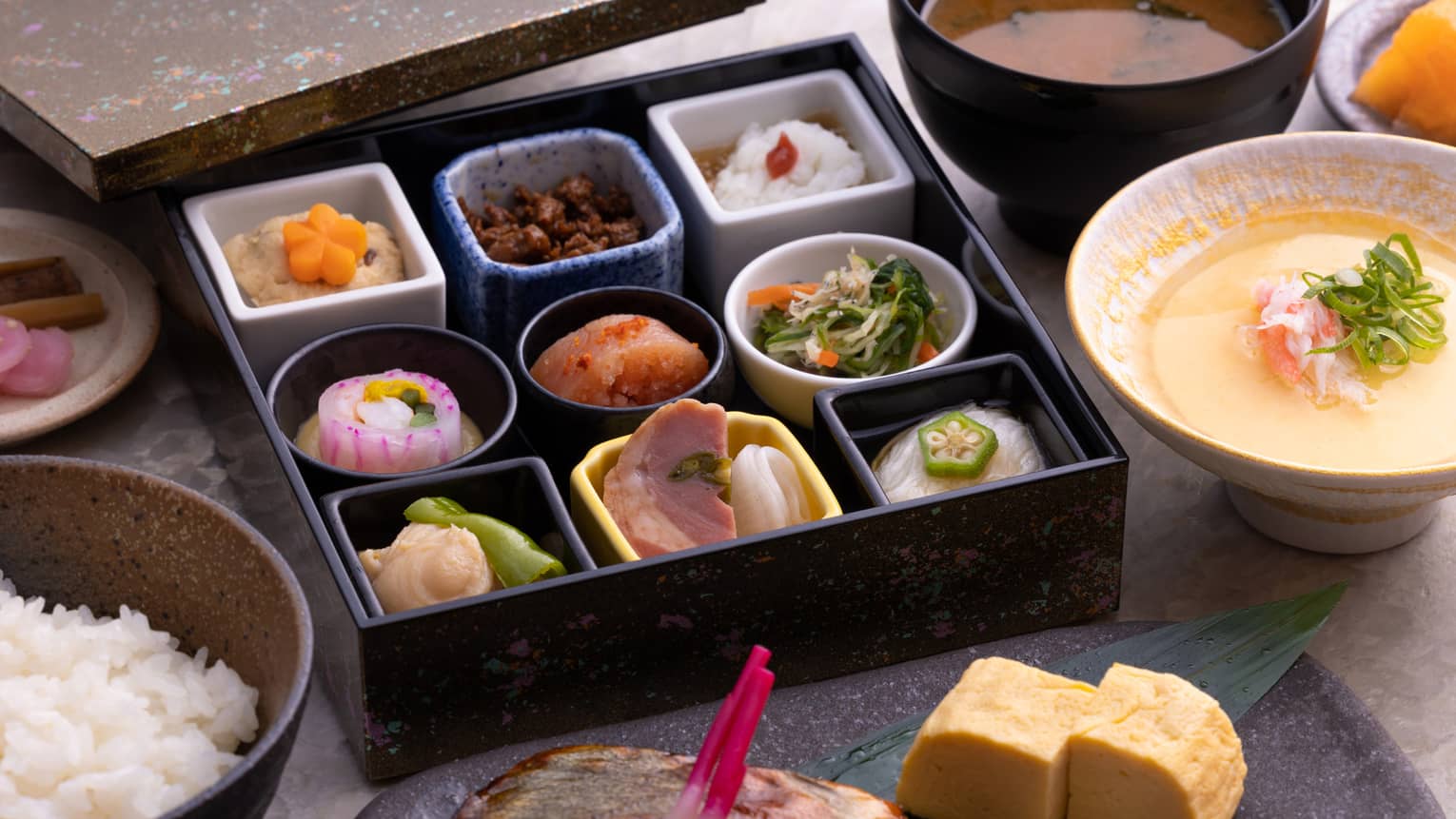 Traditional Japanese bento box breakfast with obanzai side dishes, tamagoyaki (Japanese rolled omelette), congee, steamed rice and miso soup