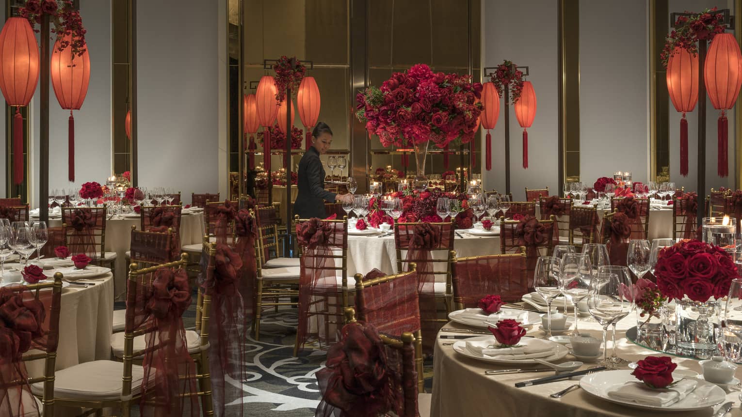Hotel staff sets large round banquet tables with red flowers, lanterns for Chinese wedding