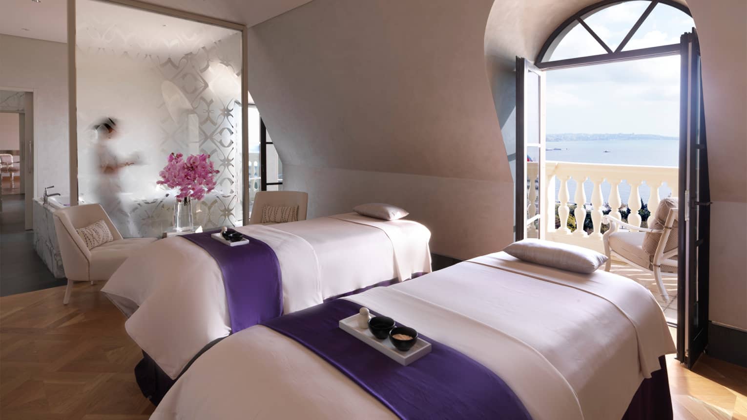 Spa with two massage beds by open balcony door overlooking ocean
