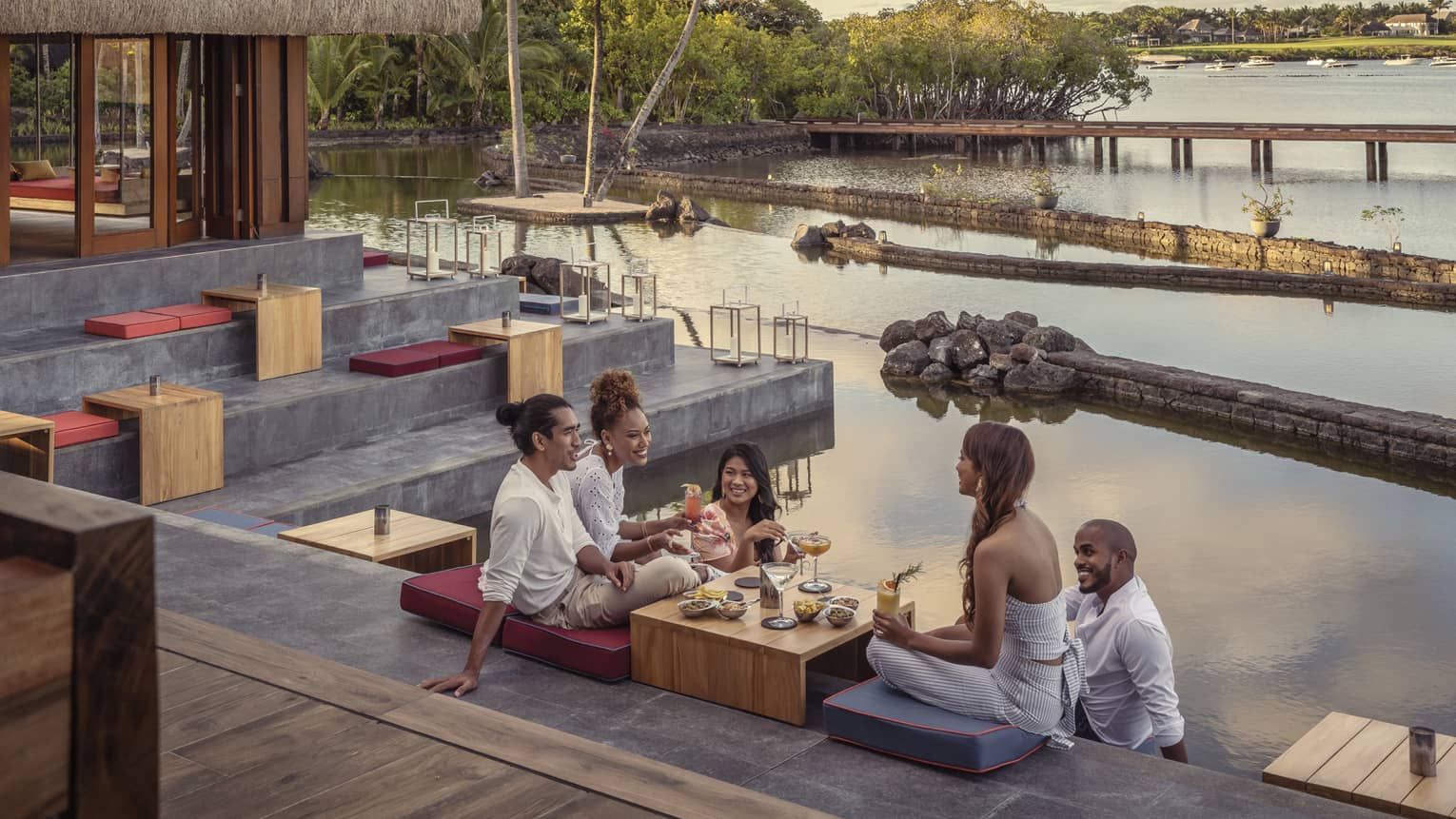 Five friends sitting and talking over food and drinks at outdoor lounge on water