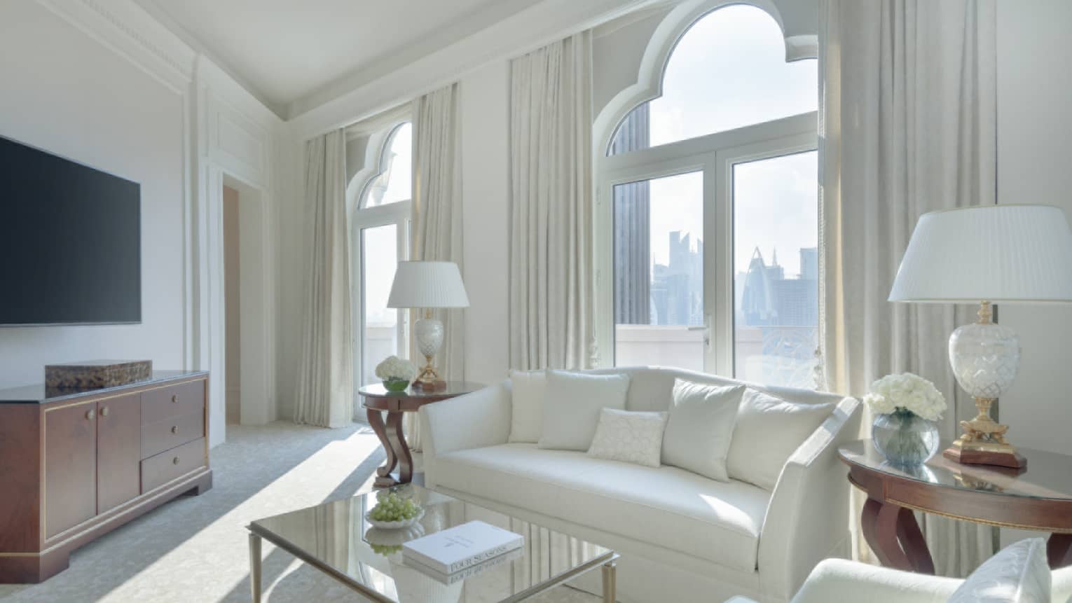 A light-filled living room with white sofa, white arm chair, tan carpet, glass coffee table, lamps