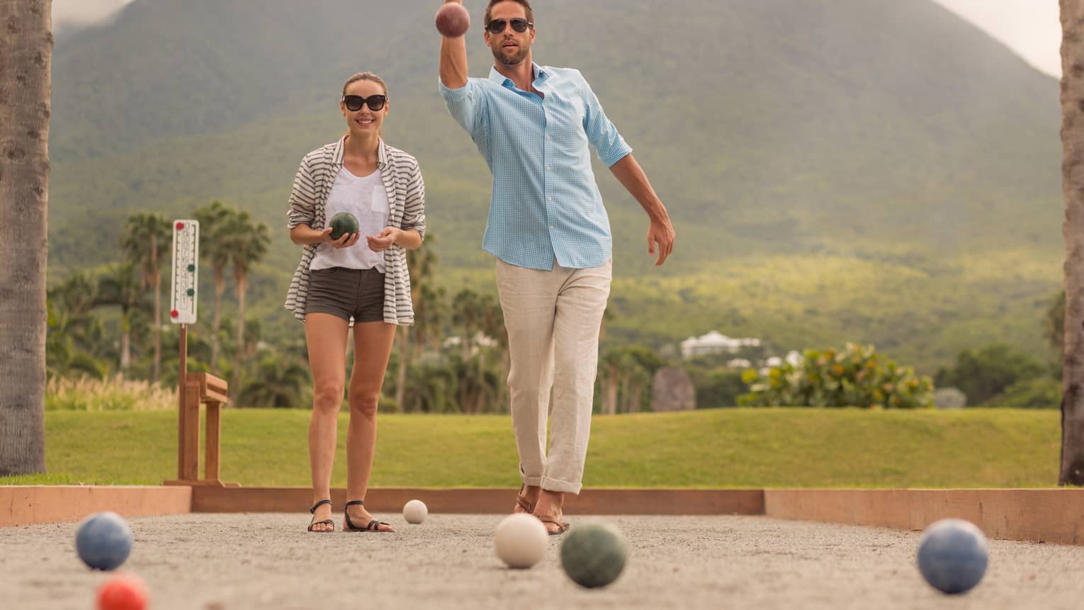 Man and woman lawn bowling, tropical mountain in background