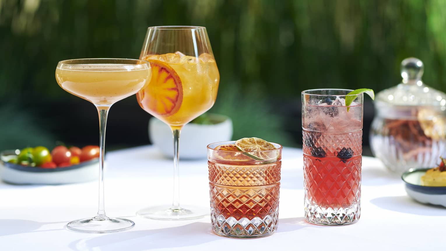A variety of cocktails on a white table that are orange or red in colour.