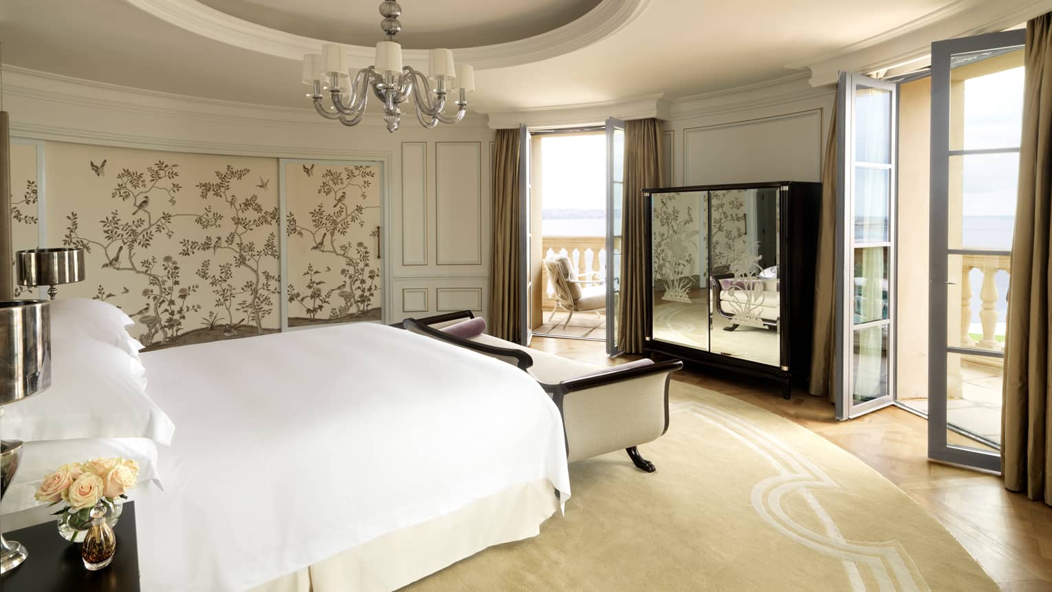 Round hotel room with recessed dome in ceiling, small chandelier, bed with white chaise, mirrored dresser, two patio doors