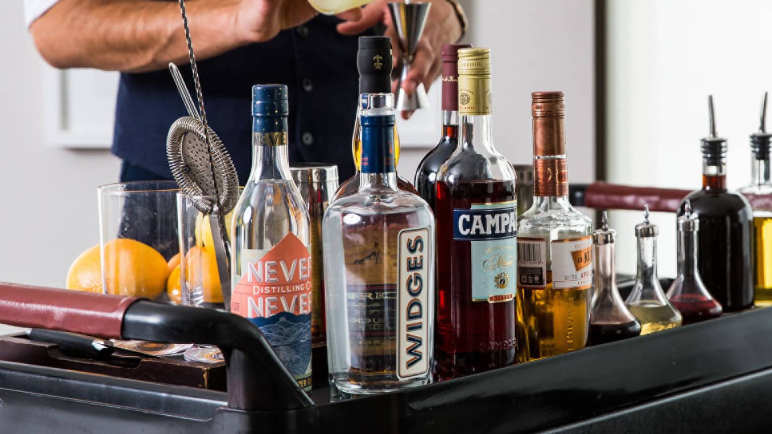 Bartender pours a cocktail at in room cocktail cart with assortment of liquor bottles