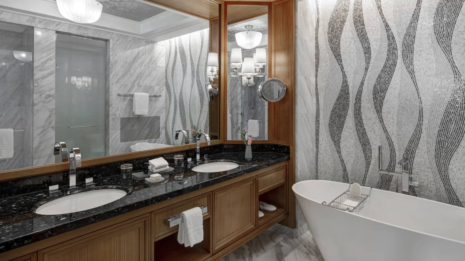 Bathroom with grey mosaic tiled wall, freestanding tub, wooden vanity with black top