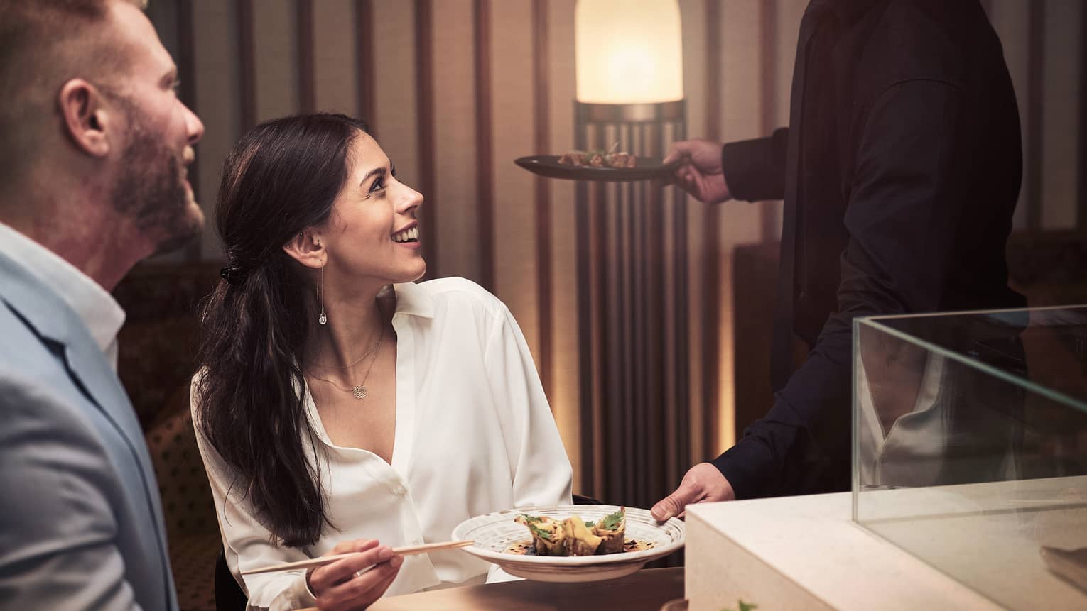 Two guests looking up at their waiter as they eat rice with chopsticks.