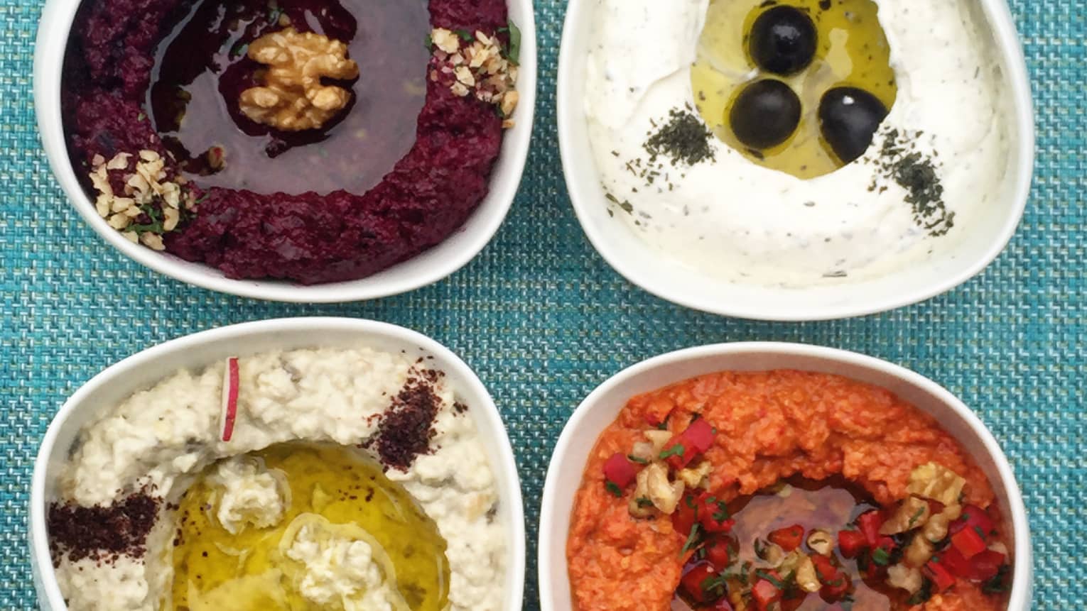Four bowls with different flavours of hummus, black olive, sesame seed, pomegranate and paprika