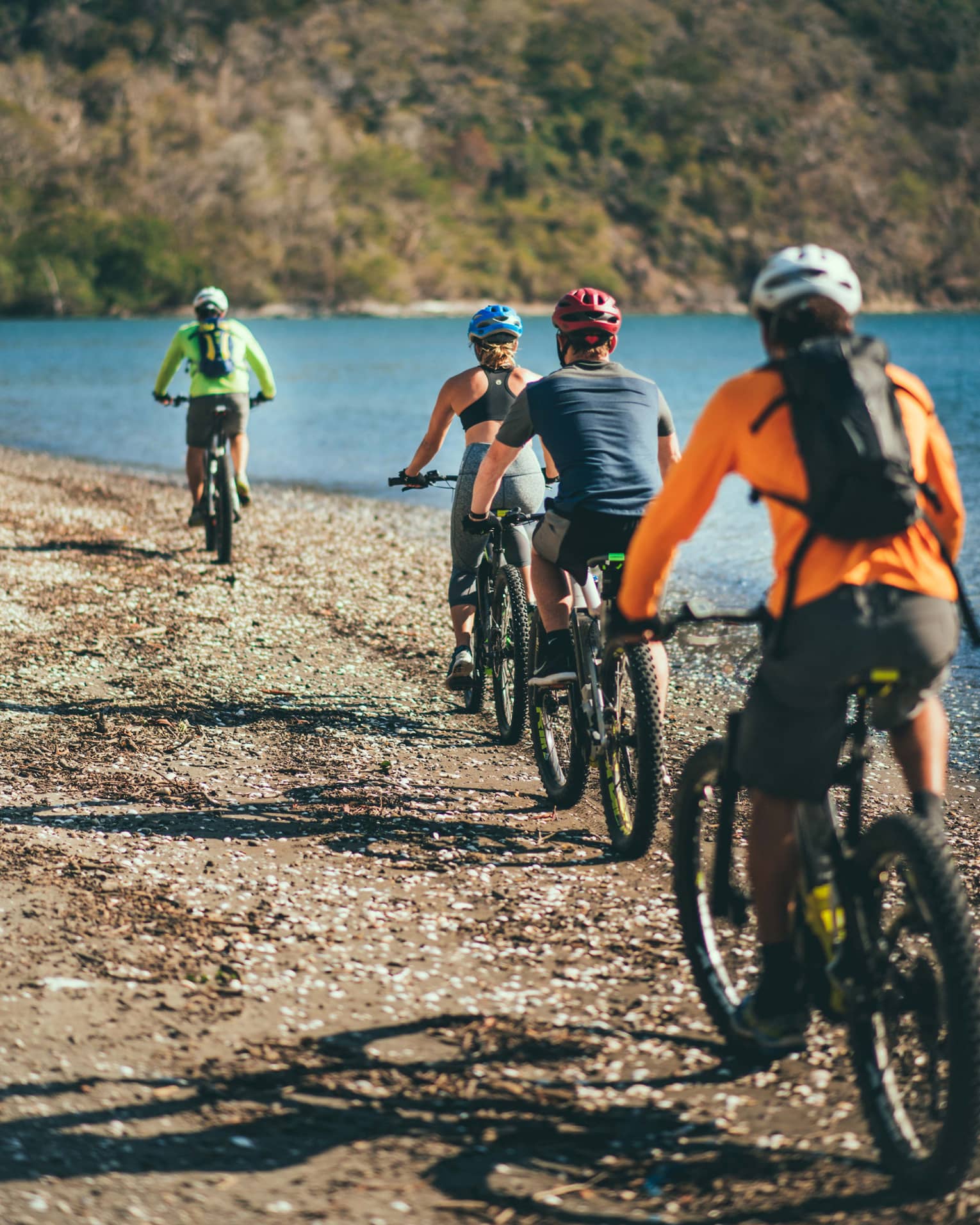 Four people riding bicycles through a rocky terrain next to the ocean
