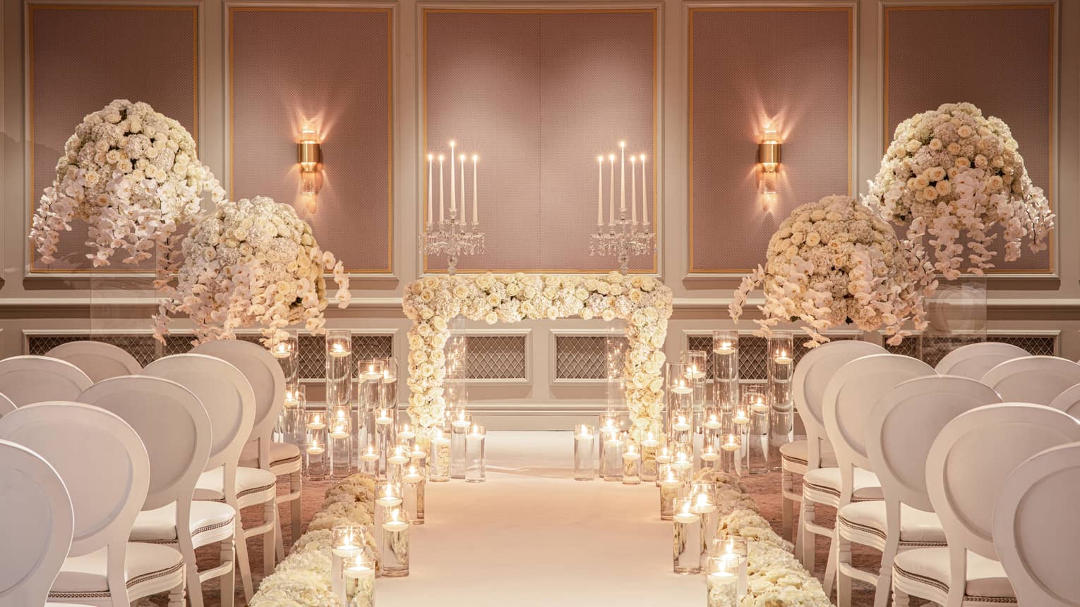 Wedding ceremony set up in event room, glowing candles line aisle with rows of white chairs facing altar