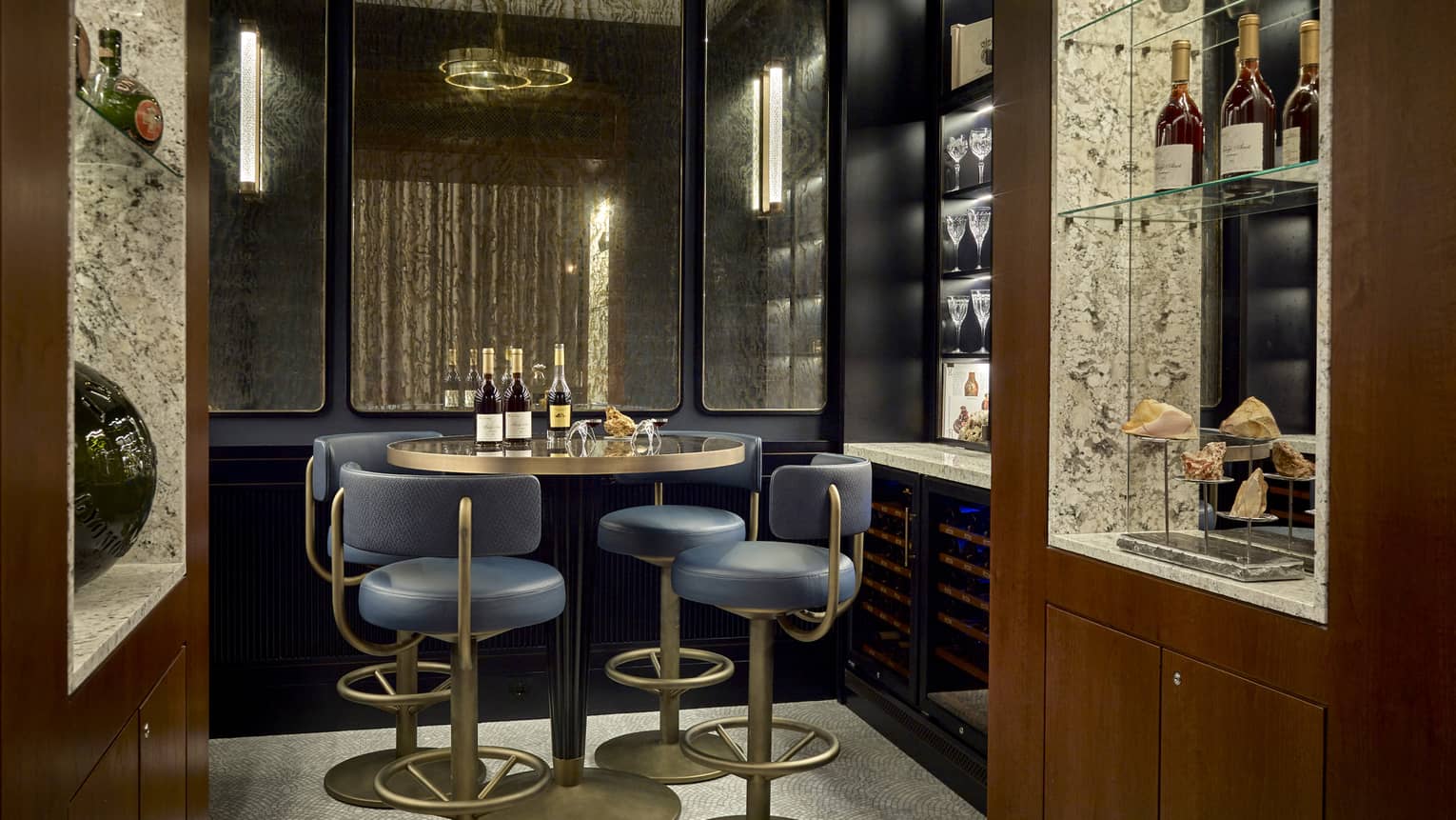 Dark private lounge area with navy and gold barstools at round high-top gold table, wine bottles