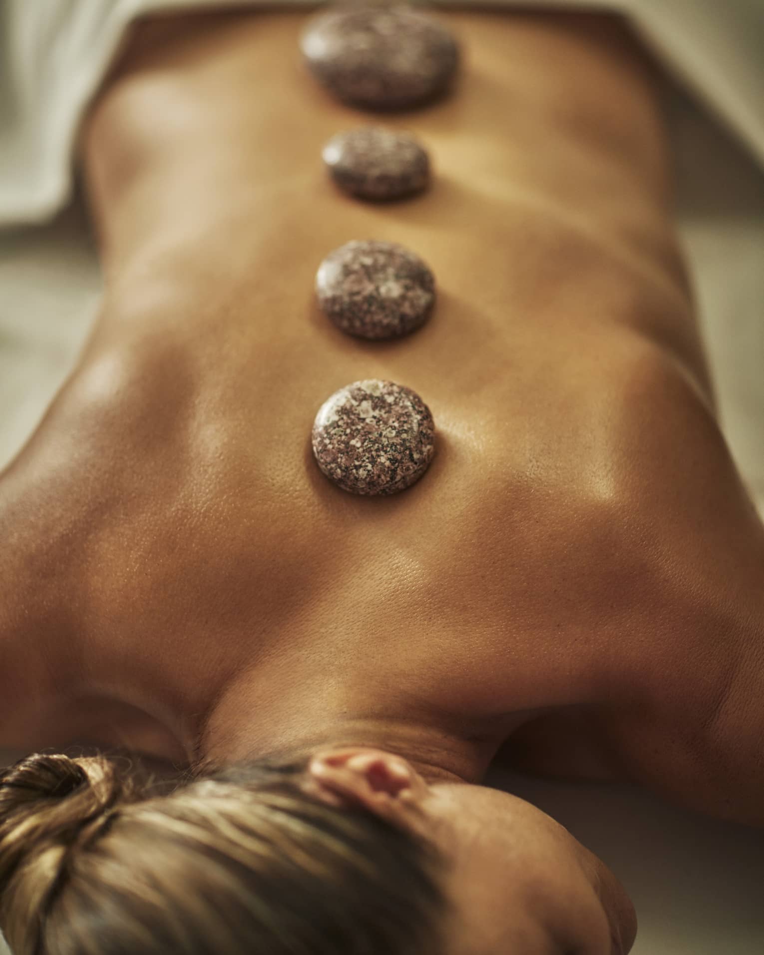 A woman lies on a spa table with four hot stones laid on her back